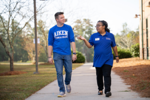 Two students walking outside and both are wearing blue shirts